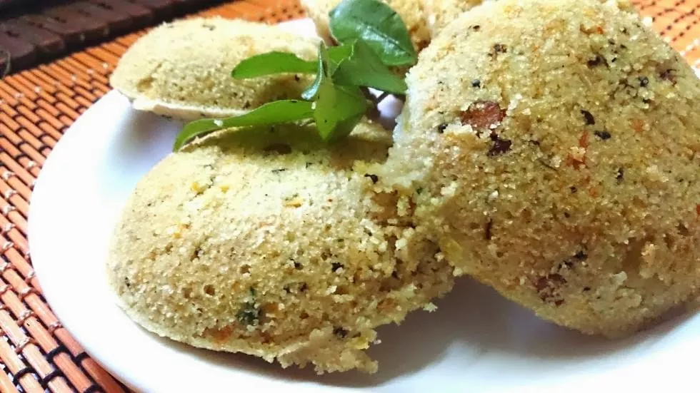 Kodo millet idly served in a plate with curry leaves on the top