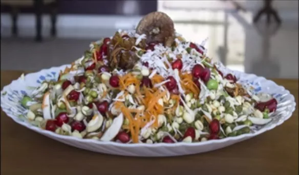 A plate full of fruit & nut sprout salad topped with pomegranate seeds, almond & cashew